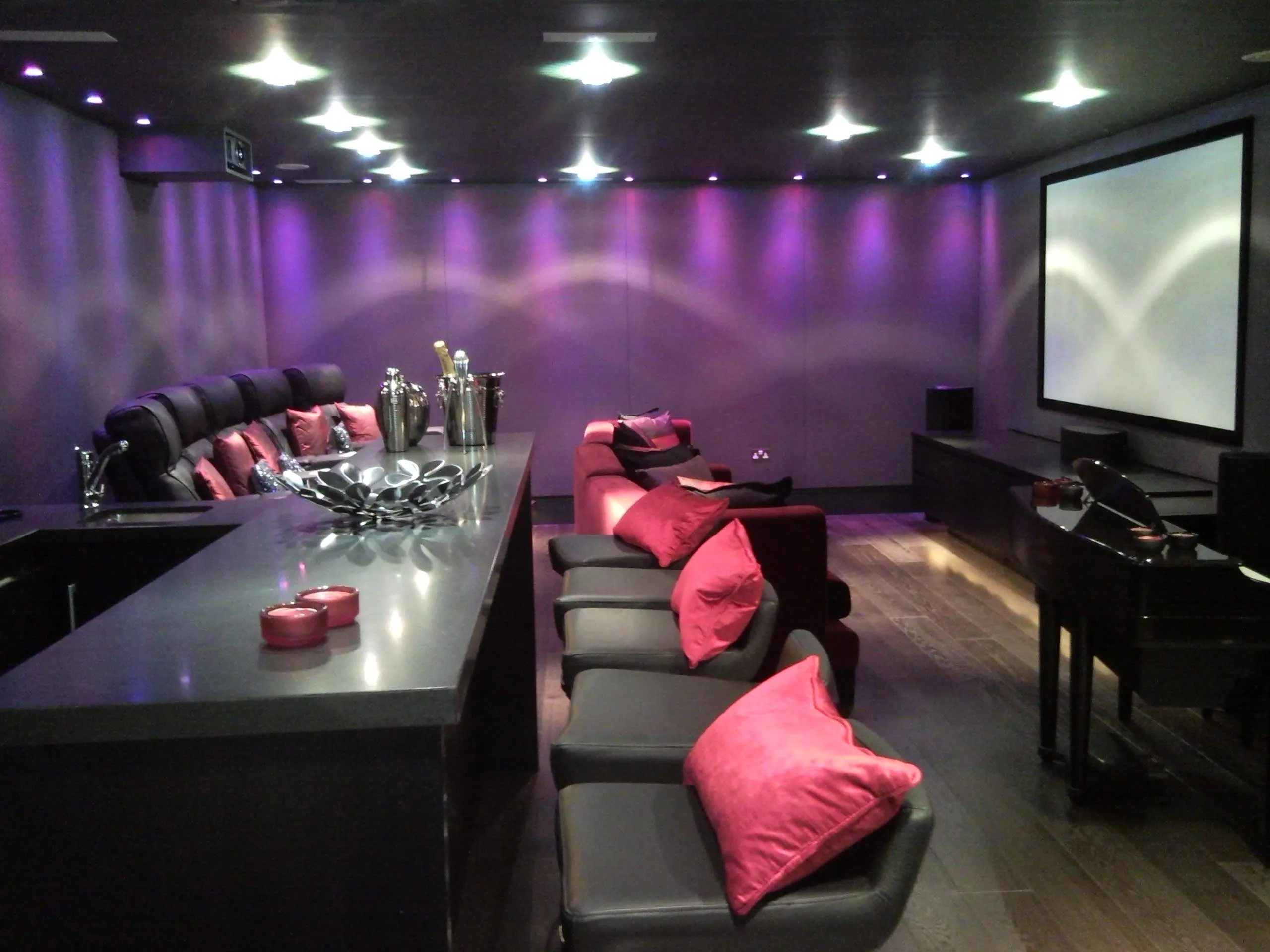 Modern lounge with purple lighting, sleek furniture, and a large projector screen