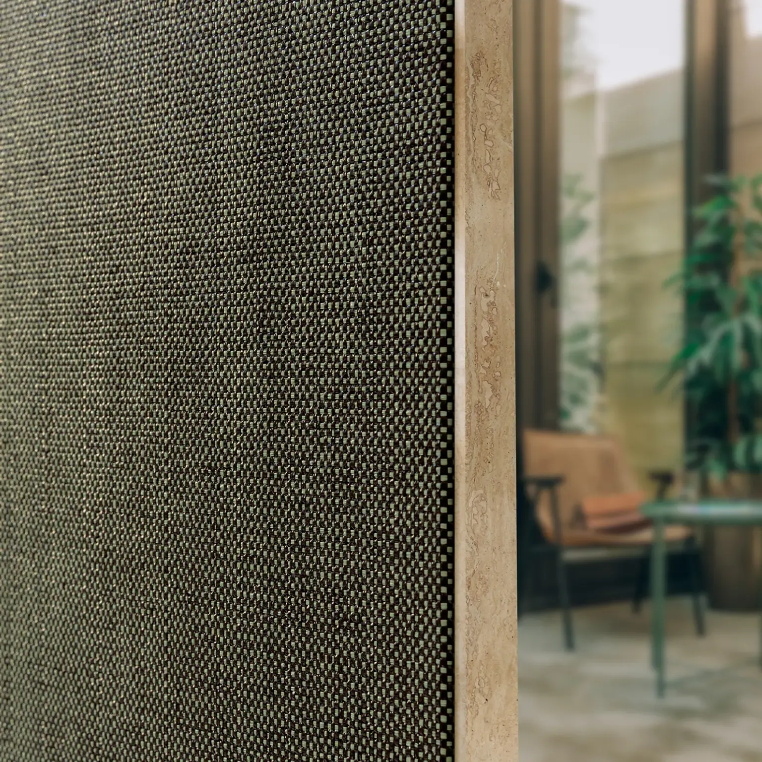Close-up of a textured wall panel beside a modern interior with plants and furniture