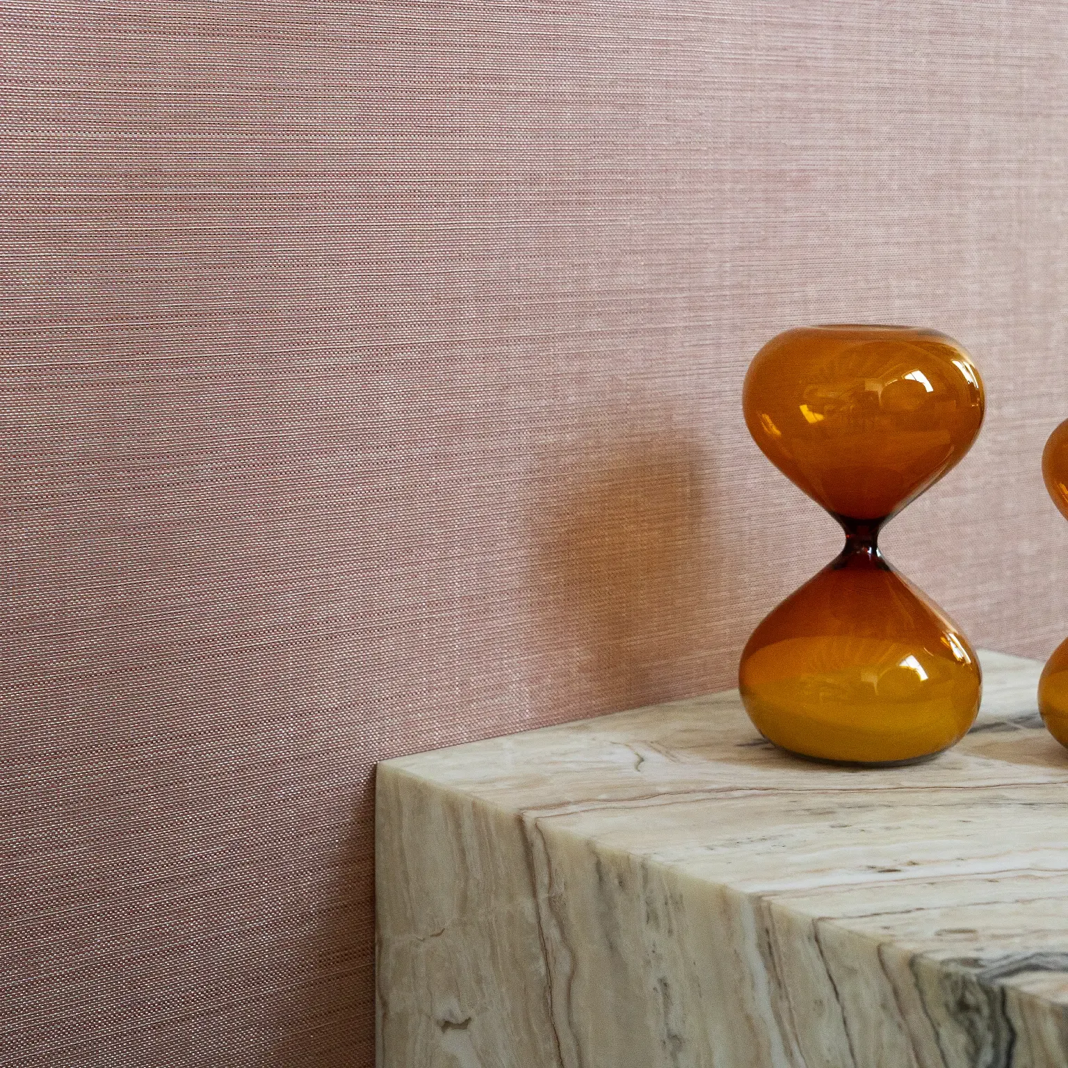 Two amber decorative vases on a marble tabletop against a pink textured wall